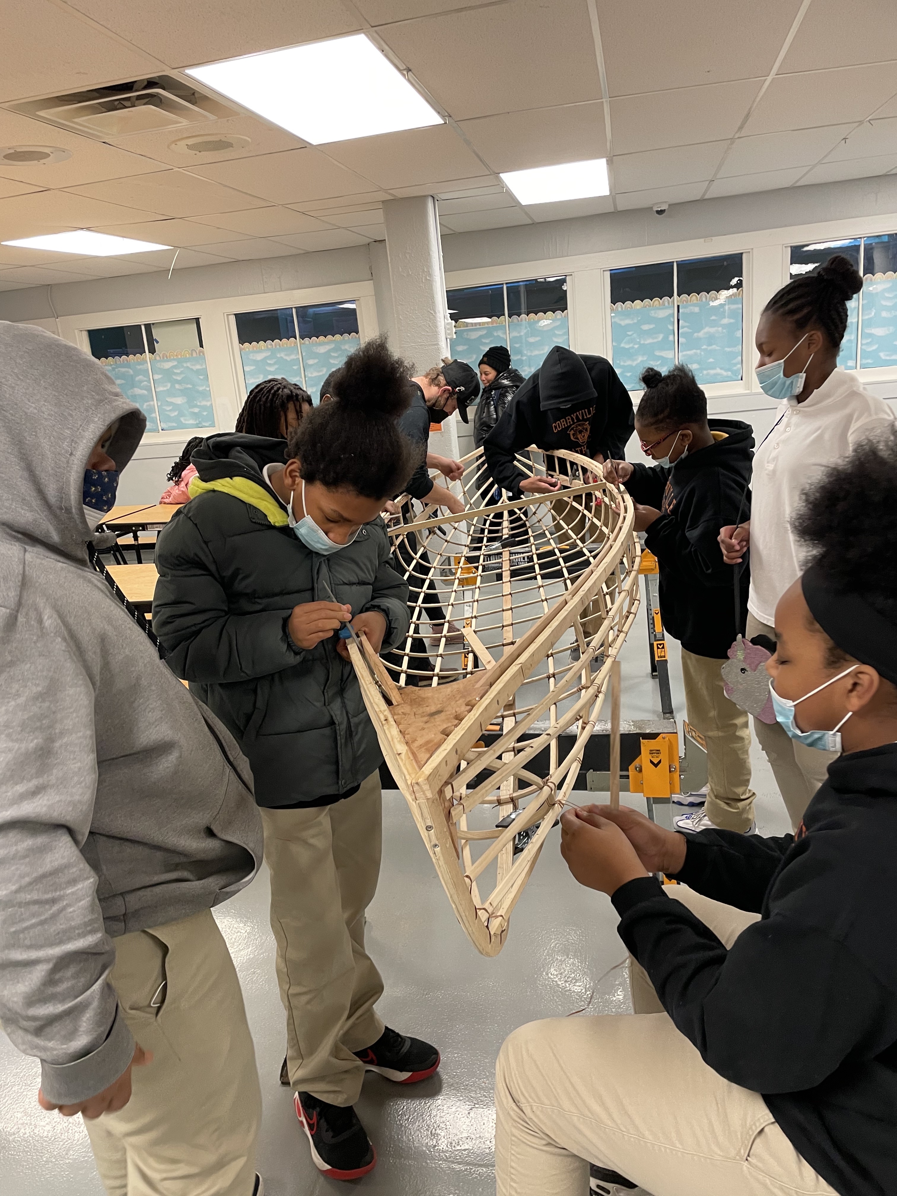 A group of students gathers around a partially built canoe 